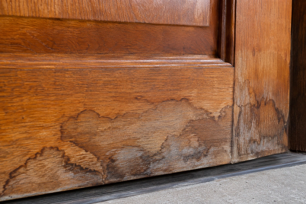 Close-up of water staining on a wood door bottom rail before restaining